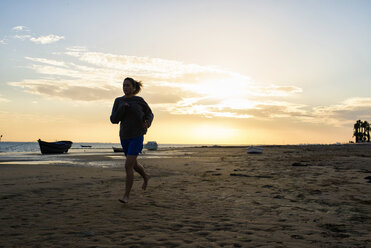 Spanien, Puerto Real, Frau joggt bei Sonnenuntergang am Strand - KIJF000043