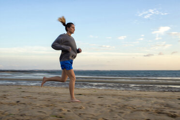 Spanien, Puerto Real, Frau beim Joggen am Strand in der Abenddämmerung - KIJF000044