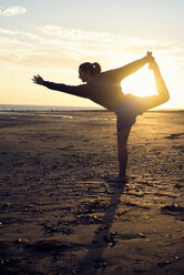 Spanien, Puerto Real, Silhouette einer jungen Frau beim Yoga am Strand bei Sonnenuntergang - KIJF000051