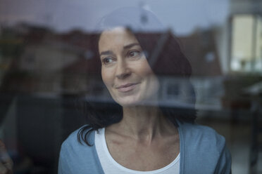 Lächelnde Frau hinter Fensterscheibe schaut hinaus - RBF003664