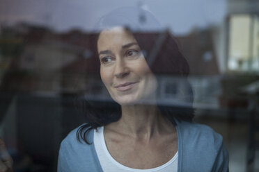 Smiling woman behind windowpane looking out - RBF003664