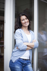 Portrait of smiling woman leaning against balcony door - RBF003668