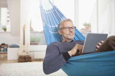 Älterer Mann zu Hause in der Hängematte liegend mit digitalem Tablet - RBF003677