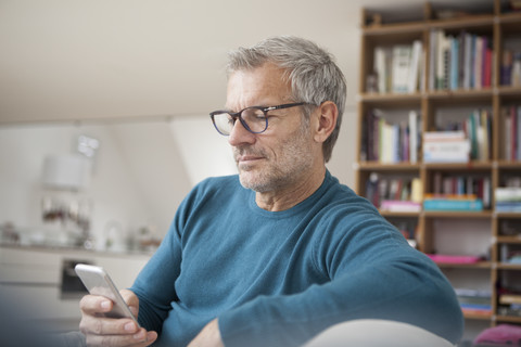 Mature man at home looking at cell phone stock photo