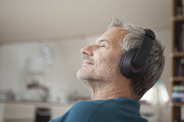 Entspannter Mann zu Hause, der Kopfhörer trägt und Musik hört - RBF003694