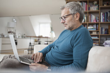 Älterer Mann sitzt zu Hause auf der Couch und benutzt einen Laptop - RBF003698