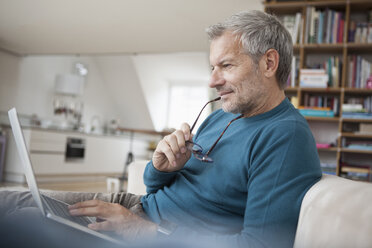 Mature man at home sitting on couch using laptop - RBF003699