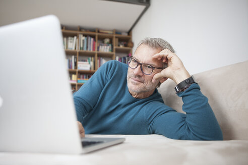 Älterer Mann zu Hause auf der Couch liegend mit Laptop - RBF003700