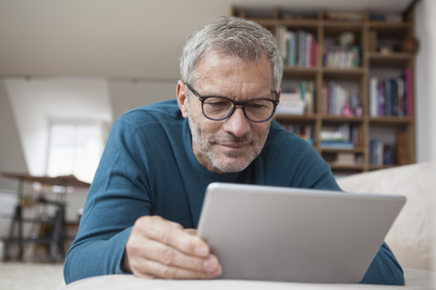 Älterer Mann zu Hause auf der Couch liegend mit digitalem Tablet, lizenzfreies Stockfoto