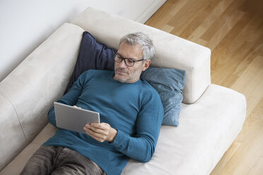 Älterer Mann zu Hause auf der Couch liegend mit digitalem Tablet - RBF003706