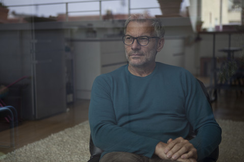 Älterer Mann sitzt hinter einer Fensterscheibe und schaut hinaus, lizenzfreies Stockfoto