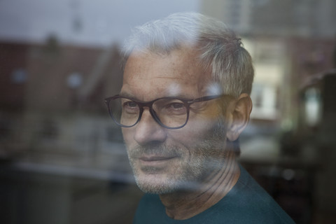 Älterer Mann hinter Fensterscheibe schaut hinaus, lizenzfreies Stockfoto