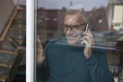 Lächelnder Mann hinter einer Fensterscheibe am Handy - RBF003709