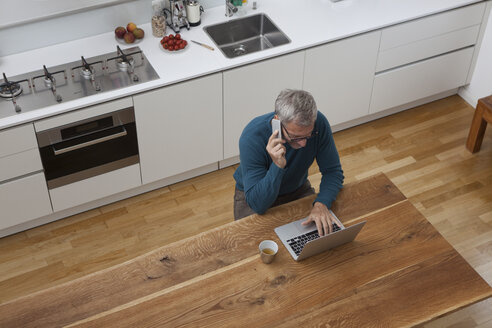 Älterer Mann in der Küche mit Handy und Laptop - RBF003722