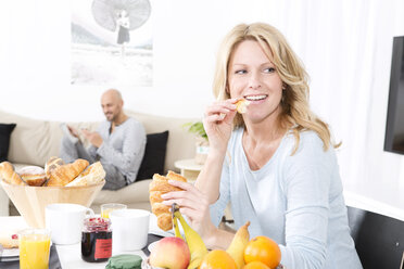 Mature woman having breakfast while man is talking at the phone - MAEF011153