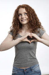 Portrait of smiling redheaded teenage girl shaping heart with her fingers - GDF000942