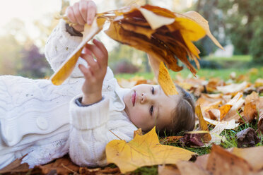 Mädchen liegt auf einer herbstlichen Wiese und hält Blätter - HAPF000081