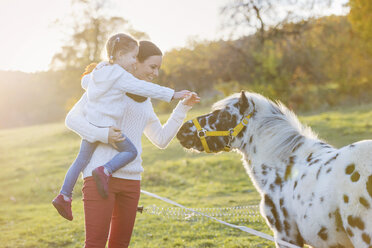 Mother with daughter petting pony on paddock - HAPF000084