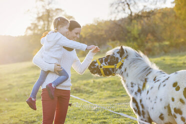 Mutter mit Tochter streichelt Pony auf der Koppel - HAPF000084