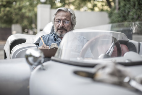 Älterer Mann mit Klemmbrett im Sportwagen, lizenzfreies Stockfoto