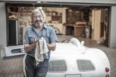 Smiling senior man with cleaning cloth leaning at sports car - ZEF007662