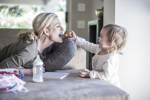 Baby Mädchen füttert Mutter mit Apfel zu Hause, lizenzfreies Stockfoto