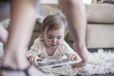 Baby girl at home lying on floor looking at digital tablet - ZEF007677