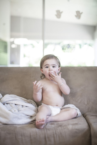 Kleines Mädchen sitzt auf der Couch und trägt eine Windel, lizenzfreies Stockfoto