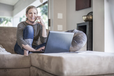 Frau sitzt mit Handy und Laptop auf der Couch - ZEF007682