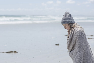 Woman wearing beanie and wrap on the beach - ZEF007719