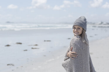 Portrait of smiling woman wearing beanie and wrap on the beach - ZEF007720