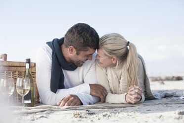 Laughing couple lying on a blanket on the beach having picnic - ZEF007725