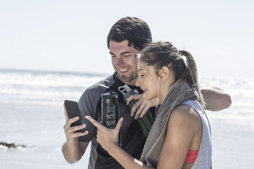 Sportlicher Mann und Frau am Strand schauen auf ihr Handy - ZEF007737