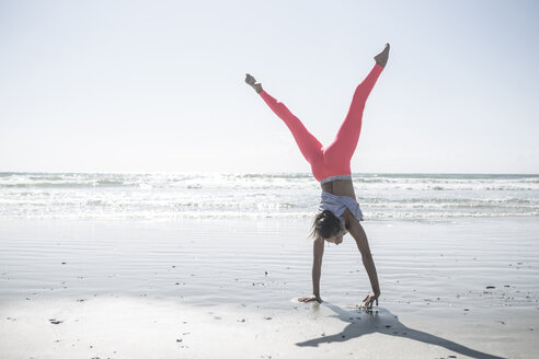 Junge Frau trainiert am Strand und macht einen Handstand - ZEF007741