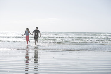 Junger Mann und Frau laufen Hand in Hand im Meer - ZEF007745