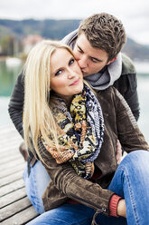 Junges Paar, das sich küsst, auf der Promenade sitzend, an einem See - DAWF000383