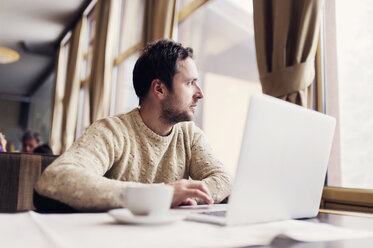 Mann mit Laptop sitzt in einem Café und schaut durch das Fenster - HAPF000096