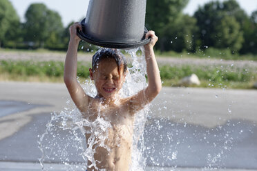 Junge, der sich im Sommer mit einem Eimer Wasser bespritzt - LBF001317