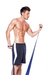 Hemdfreier muskulöser Mann beim Training mit Fitnessband vor weißem Hintergrund - DAWF000394