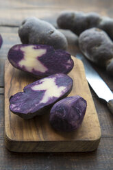 Sliced and whole purple potatoes on wooden board - SARF002400