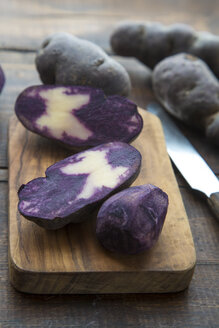 Geschnittene und ganze violette Kartoffeln auf Holzbrett - SARF002400