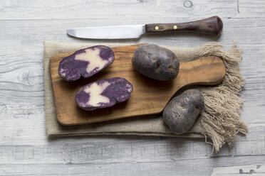 Geschnittene und ganze violette Kartoffeln auf Holzbrett und Tuch - SARF002404