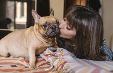 Junge Frau küsst ihre französische Bulldogge auf dem Bett sitzend - GEMF000574