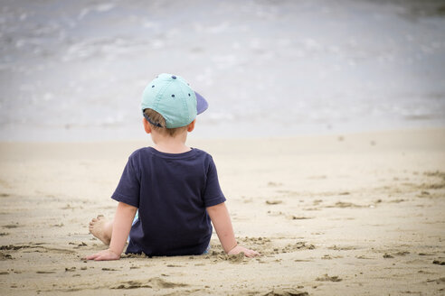 Rückansicht eines kleinen Jungen am Strand sitzend am Meer - ABAF001968