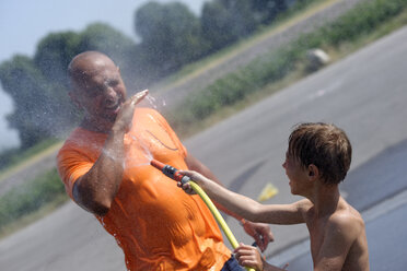 Junge bespritzt seinen Vater mit Wasser aus dem Gartenschlauch - LBF001324
