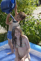 Kleiner Junge gießt Wasser auf seine Schwester mit Gießkanne im Sommer - LBF001327