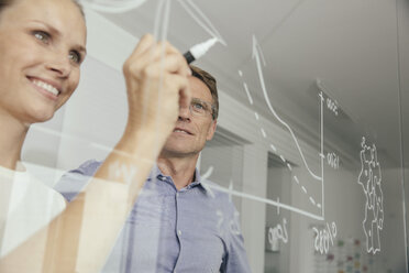 Young woman writing onto glass wall in office - MFF002528