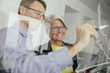 Man writing onto glass wall in office - MFF002532