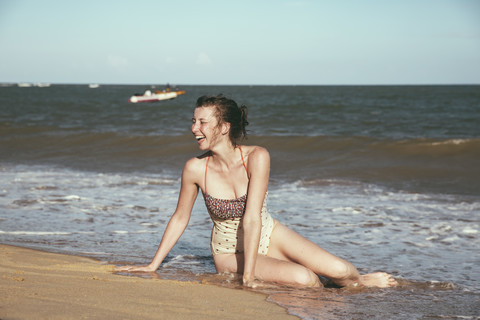 Brasilien, Bahia, lachende Frau am Meer sitzend, lizenzfreies Stockfoto