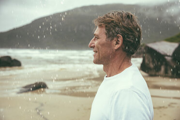 Brasilien, Florianopolis, Profil eines glücklichen Mannes, der im Regen am Strand steht - MFF002568